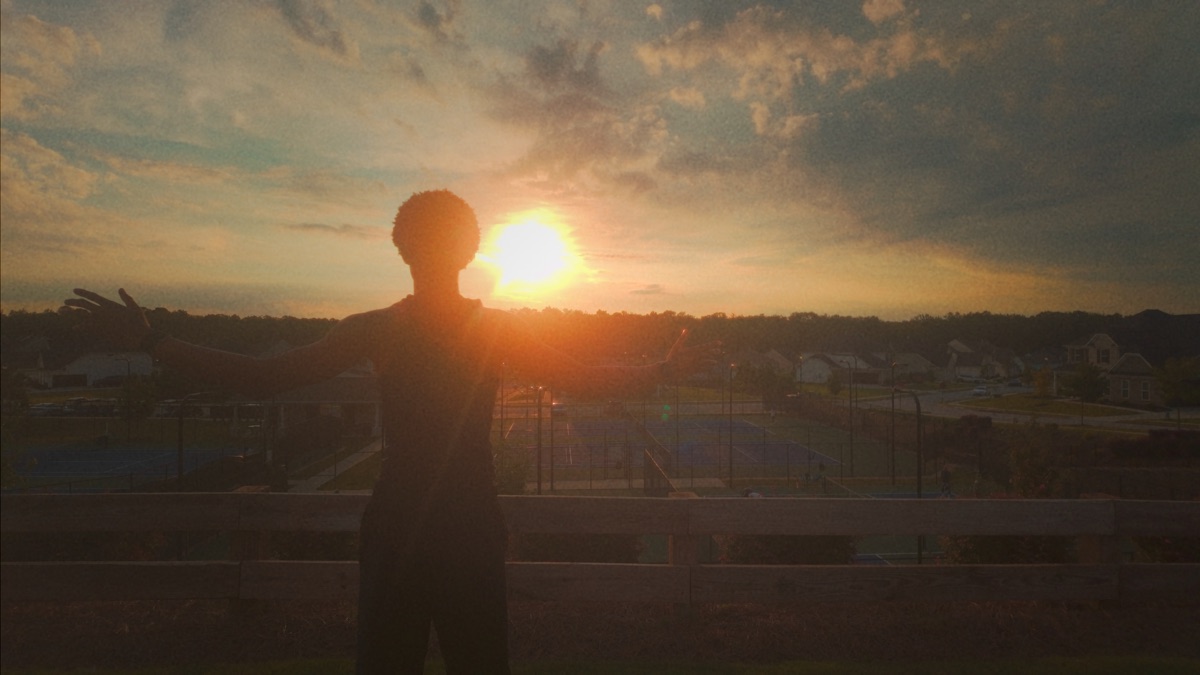 Kam standing with his arms open in front of a sunset
